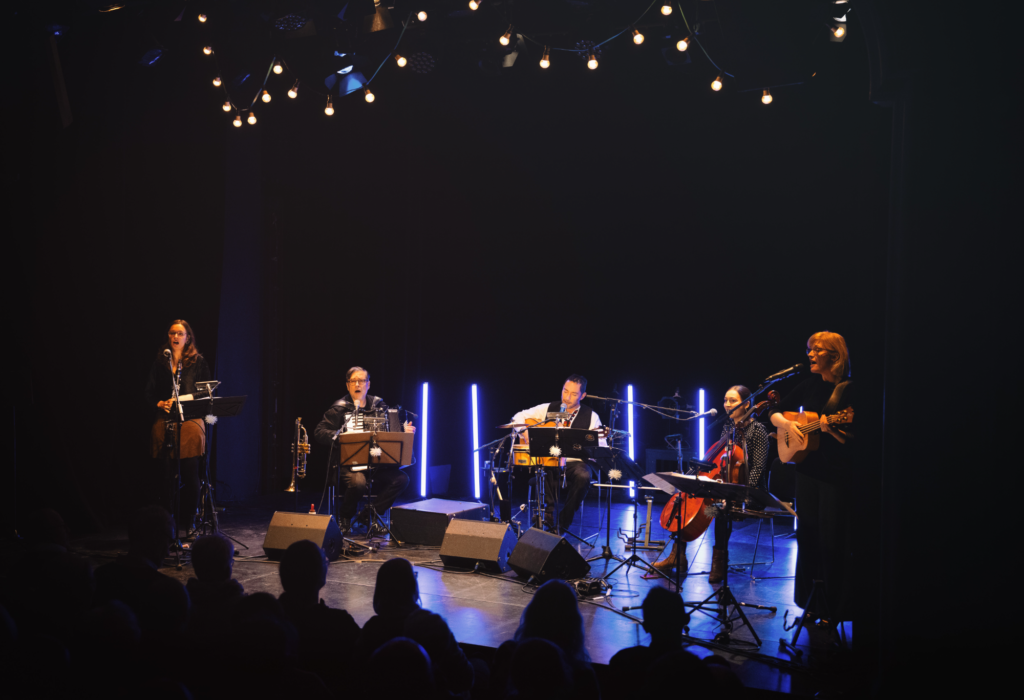 5 Musiker auf der Bühne mit Gitarre Akkordeon Klarinette Cello und Geige und sie singen